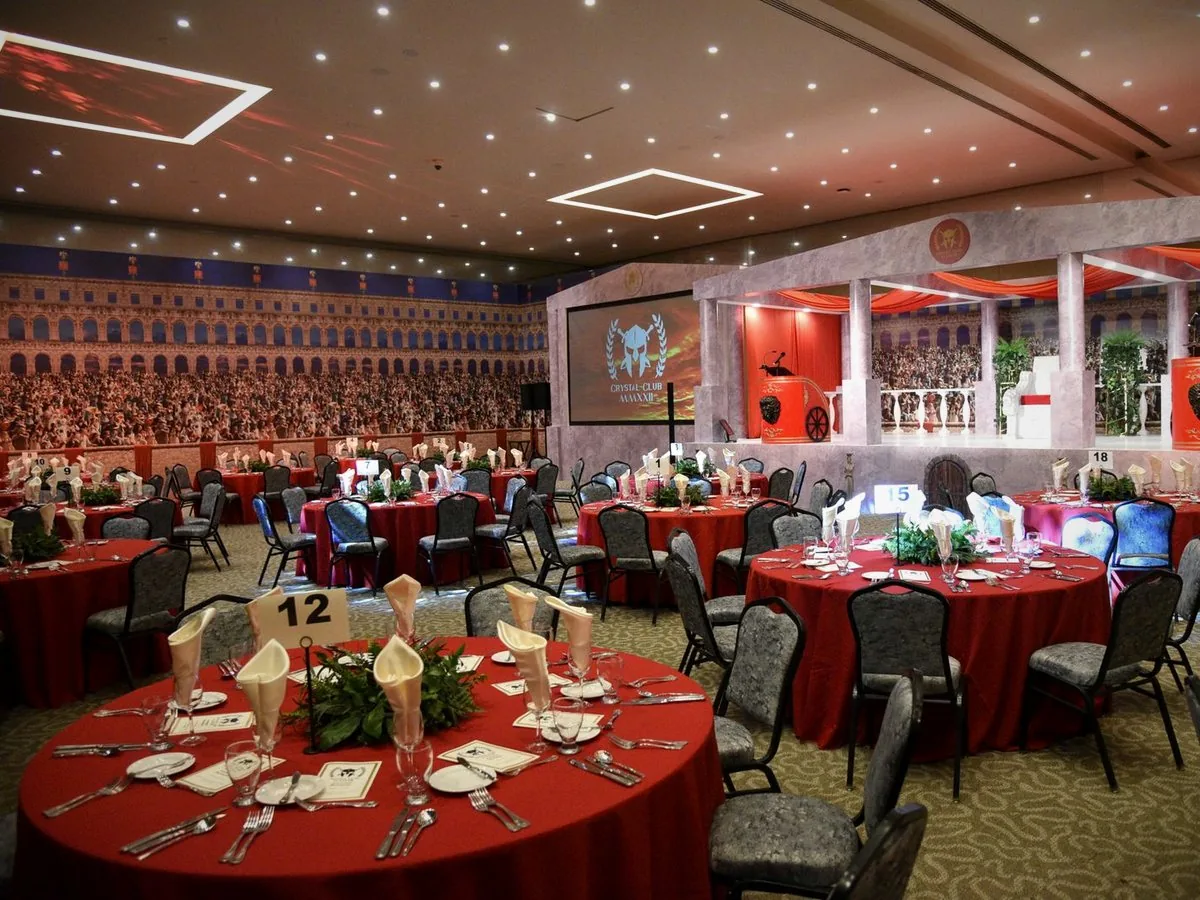 A gala hall set for a showcase dinner, with red tables and a stage screen